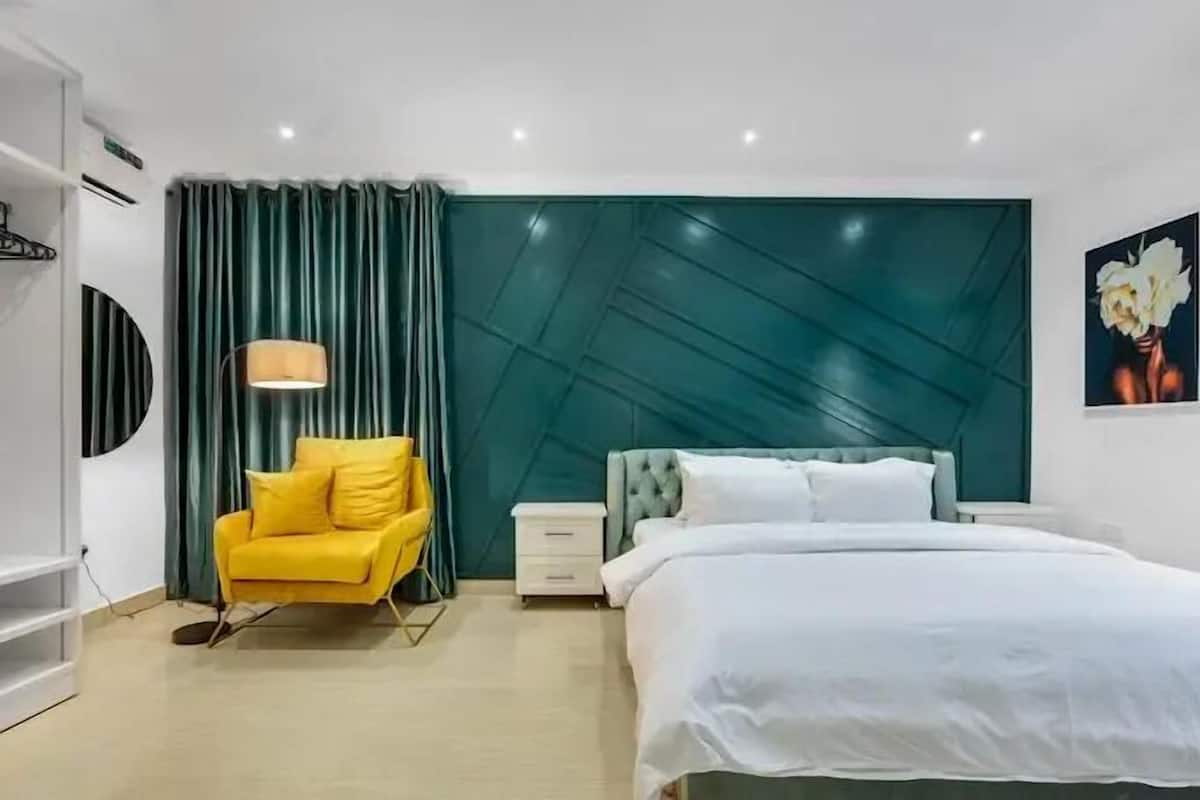 A modern bedroom with a bed, a yellow armchair, a nightstand, and a wall-mounted lamp.