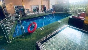 Piscina interior com cobertura de vidro, rodeada por um edifício com várias janelas e unidades de ar condicionado.