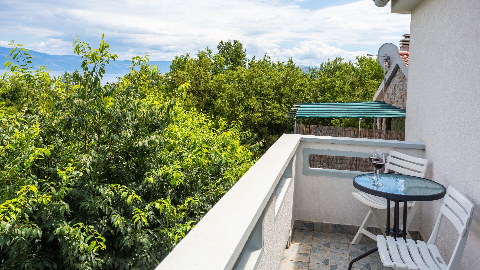 A balcony with a table and chairs, surrounded by lush greenery and a view of distant mountains.