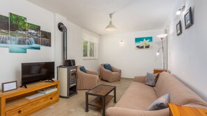 A living room with a TV, sofa, armchair, fireplace, and artwork on the walls.