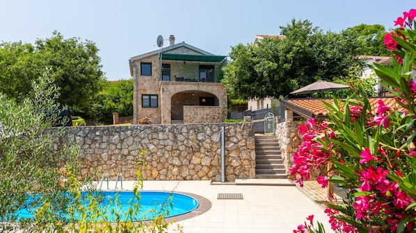 A stone house with a pool, surrounded by greenery and flowers.