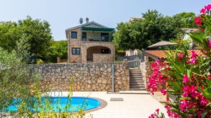 A stone house with a pool, surrounded by greenery and flowers.