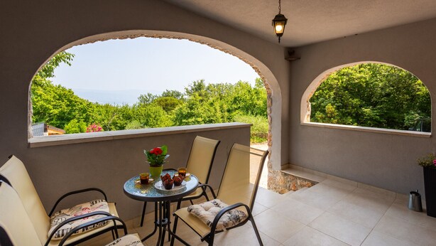 A balcony with a table and chairs, a potted plant, and a view of greenery and a distant landscape. - Villa Risika 1 with pool island Krk by Villas Guid (Risika)