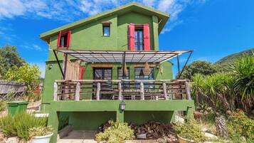 A two-story house with a balcony, green exterior walls, and a red door.