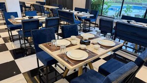 A dining area with checkered flooring, blue upholstered chairs, and tables set with plates, glasses, and cutlery. - Aryston Hotel Udaipur (Udaipur)
