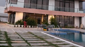 A multi-story hotel with a pool area, outdoor seating, and a clear view of the sky. - Aryston Hotel Udaipur (Udaipur)