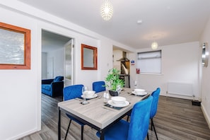 A dining area with a table set for four, blue chairs, a potted plant, and a white radiator.