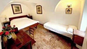 Un dormitorio con una cama individual, un escritorio de madera y una silla. Hay cuadros en las paredes y un florero con flores sobre el escritorio.