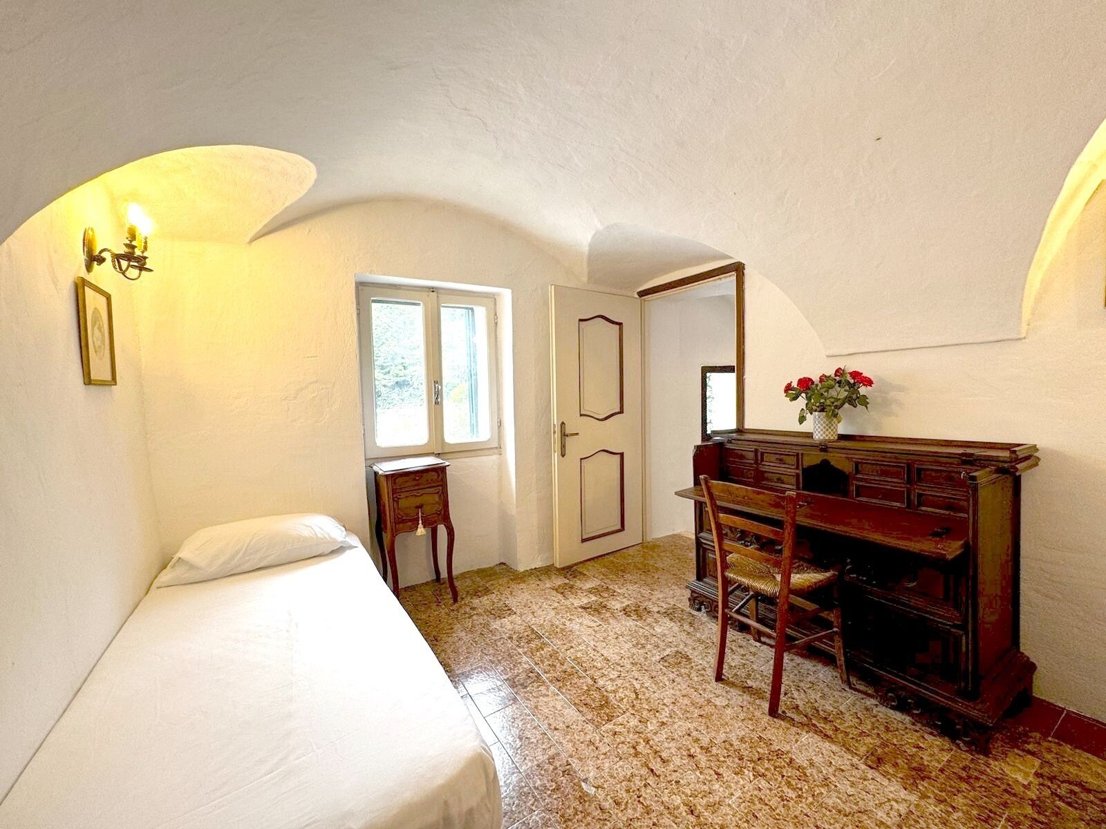 A room with a bed, a desk with a chair, a small table, and a window.