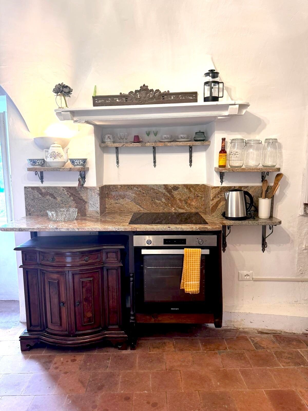 Una cocina con encimera de granito, armarios de madera oscura, horno empotrado y salpicadero blanco.