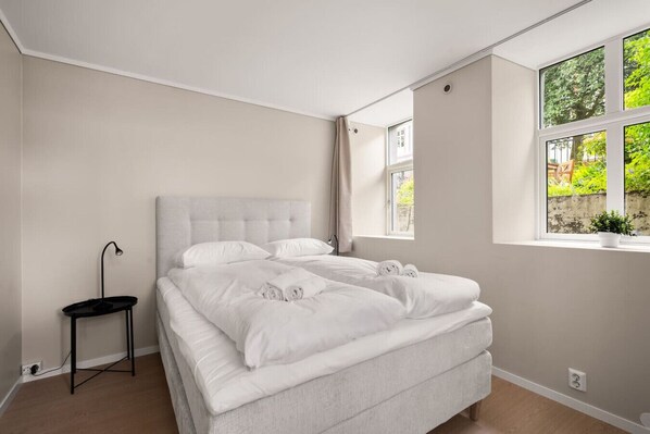 A modern bedroom with a large bed, a small side table, and a window with a view of greenery. - City Apartment I Short Walk to Sights (Bergen)