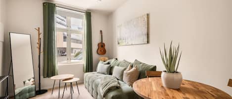 Un salon chaleureux avec un canapé vert, une table à manger en bois, une guitare et une plante en pot.