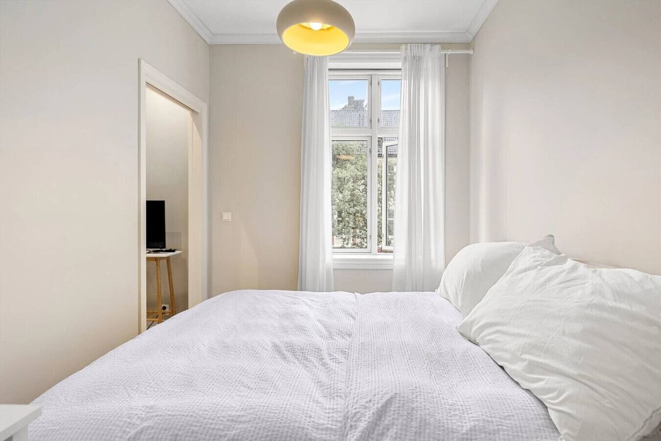 Un dormitorio con cama, televisor y ventana con cortinas.