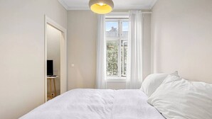 A bedroom with a bed, a television, and a window with curtains.