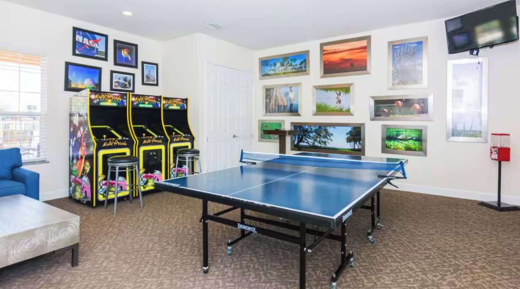 Een kamer met een tafeltennistafel, speelautomaten en ingelijste foto’s aan de muur.