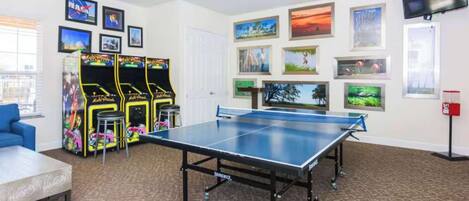 A room with a ping pong table, arcade games, and framed pictures on the walls.