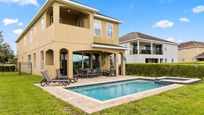 A two-story house with a swimming pool, outdoor seating, and a well-maintained lawn.