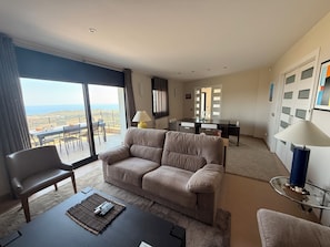 A modern living room with a sofa, a dining table, and a view of the sea. - Architect-designed home with an extraordinary panoramic view of the ocean and an infinity pool (Castell-Platja d'Aro)