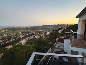 A residential area with a view of the sea and hills, featuring modern houses and a balcony with a glass railing. - Architect-designed home with an extraordinary panoramic view of the ocean and an infinity pool (Castell-Platja d'Aro)
