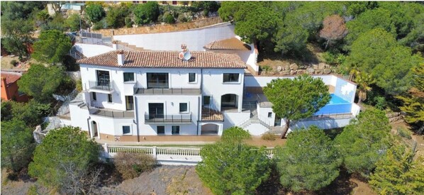 A multi-story white building with a tiled roof, surrounded by trees and a swimming pool. - Architect-designed home with exceptional panoramic ocean views and an infinity pool (Castell-Platja d'Aro)