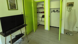 Et værelse med et fjernsyn på et stativ, en grøn garderobe og et skab med hængende tøj.