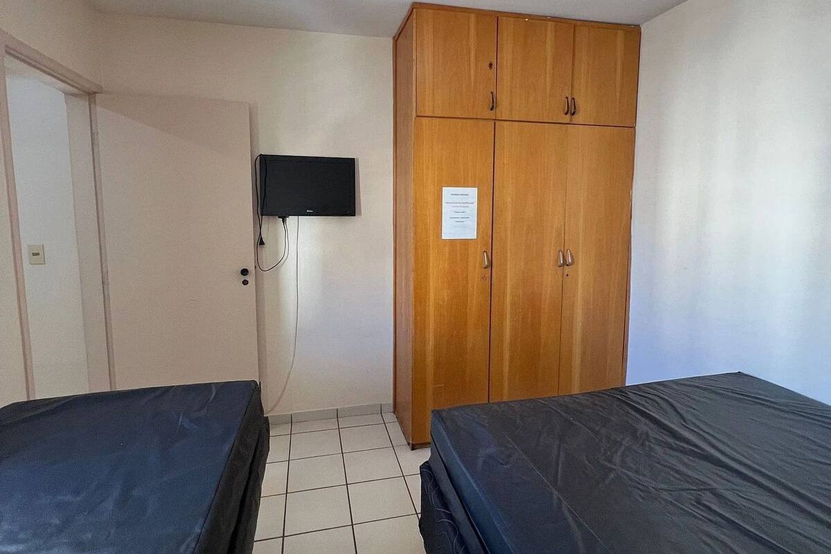 Ein Zimmer mit zwei Betten, einem Holzschrank, einem Fernseher und einer Deckenleuchte.