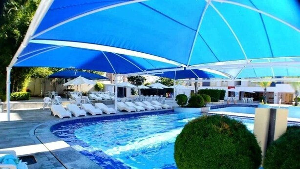 A swimming pool with lounge chairs and umbrellas, surrounded by greenery. - Eldorado Park (Caldas Novas)