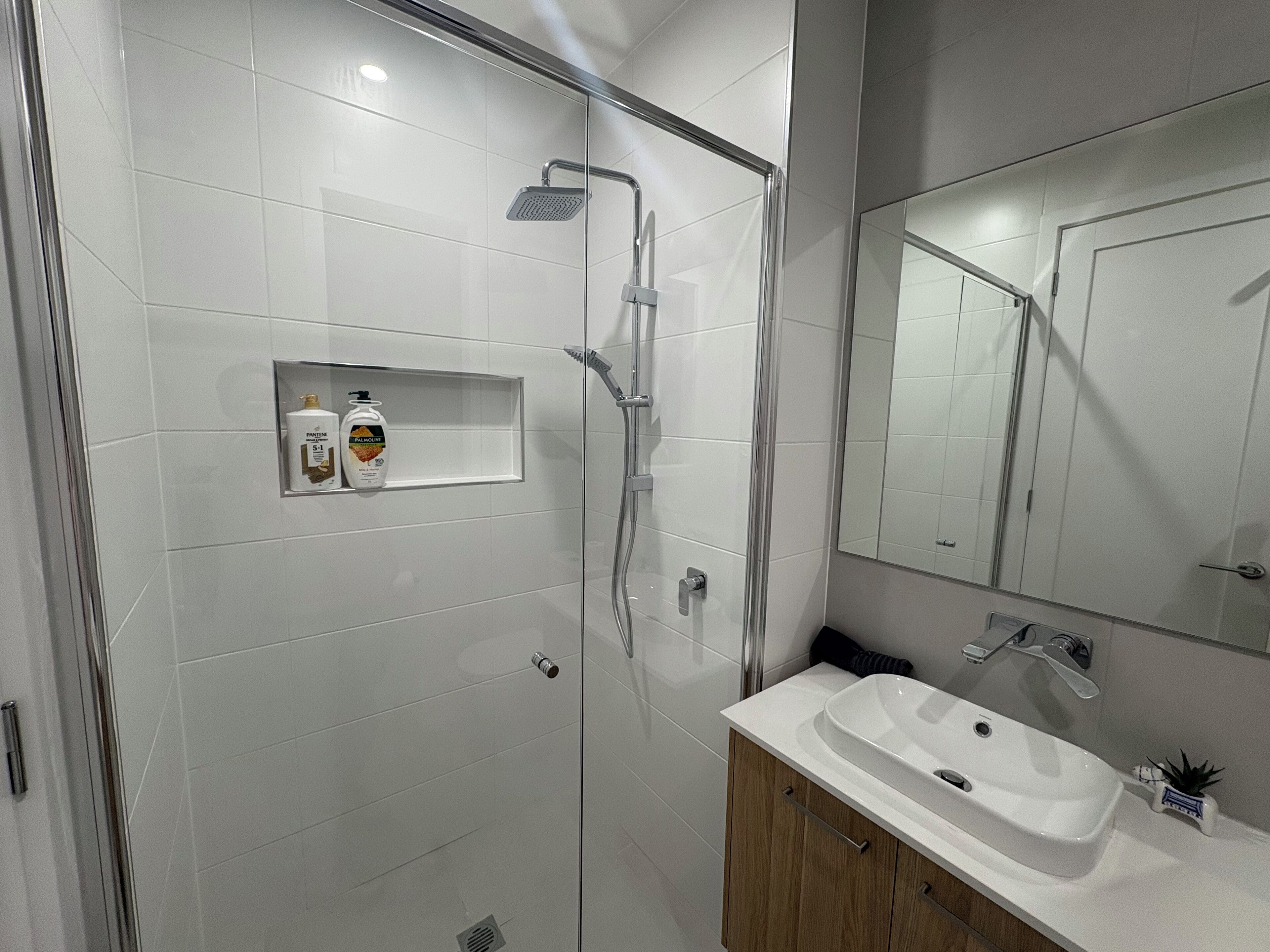 Une salle de bain moderne avec une douche à parois de verre, un lavabo blanc et un miroir au-dessus.
