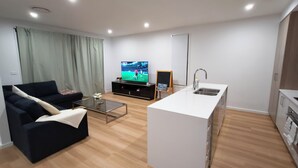 Una sala de estar moderna con un sofá negro, una mesa de centro de vidrio, un televisor y un pequeño cuadro sobre un caballete.