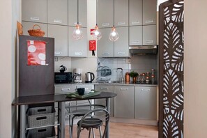 Een kleine keuken met een koelkast, magnetron, koffiezetapparaat en een eethoekje met een tafel en stoelen.