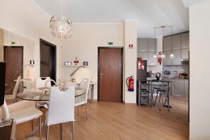 Uma cozinha moderna com eletrodomésticos de aço inoxidável, uma área de jantar com mesa de vidro e cadeiras brancas, e piso de madeira.