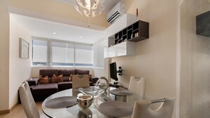 A modern living room with a glass dining table, a sofa, and a TV mounted on the wall. - Charming Studio in Faro’s Historic Center – Faro Downtown (Faro)