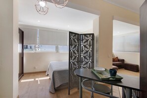 Quarto moderno com cama, mesa de jantar com bandeja, divisória decorativa e vista para o exterior.