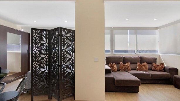A modern living room with a sectional sofa, a decorative black partition, and a dining area with a table and chairs. - Charming Studio in Faro’s Historic Center – Faro Downtown (Faro)