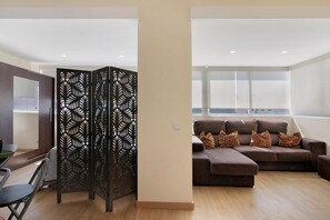 Uma sala de estar moderna com um sofá seccional, um divisório preto decorativo e uma área de jantar com mesa e cadeiras.