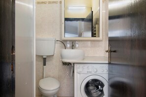 Casa de banho pequena com sanita, lavatório e máquina de lavar roupa.