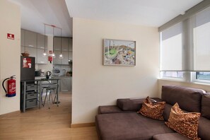 Een moderne woonkamer met een bank, een schilderij en een keuken op de achtergrond.