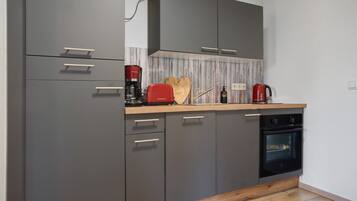 Une cuisine moderne avec des meubles gris, un plan de travail en bois, une machine à café rouge et un four encastré.