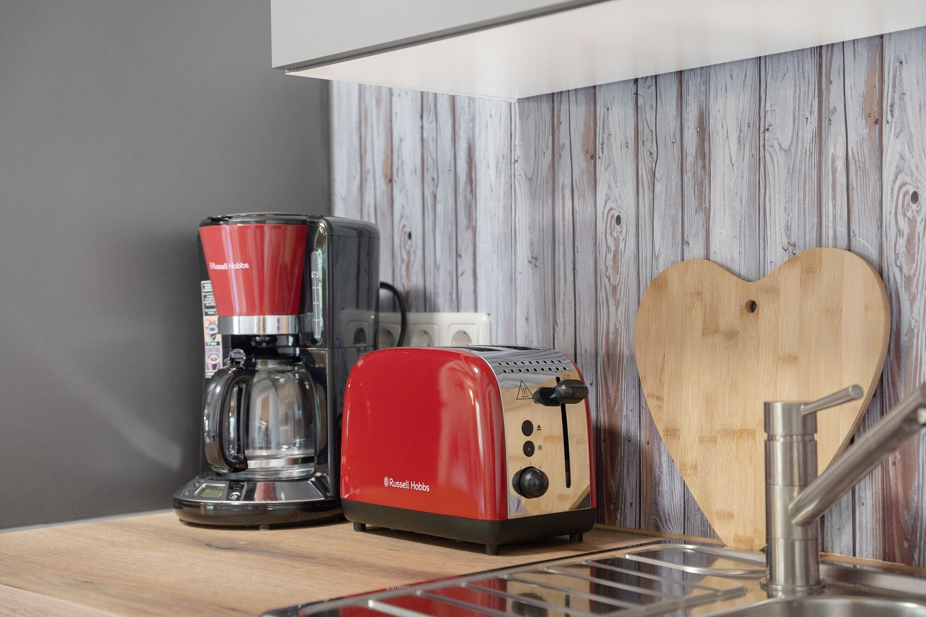A kitchen with a red toaster, a coffee maker, and a wooden heart-shaped cutting board.