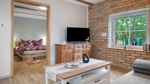 A room with a brick wall, a television on a wooden cabinet, a window with a view of greenery, and a bed with a colorful headboard. - Apartment 'Uschi' with Shared Garden and Wi-Fi (Warrenzin)