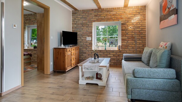 A living room with a brick wall, a television, a sofa, and a window. - Apartment 'Uschi' with Shared Garden and Wi-Fi (Warrenzin)