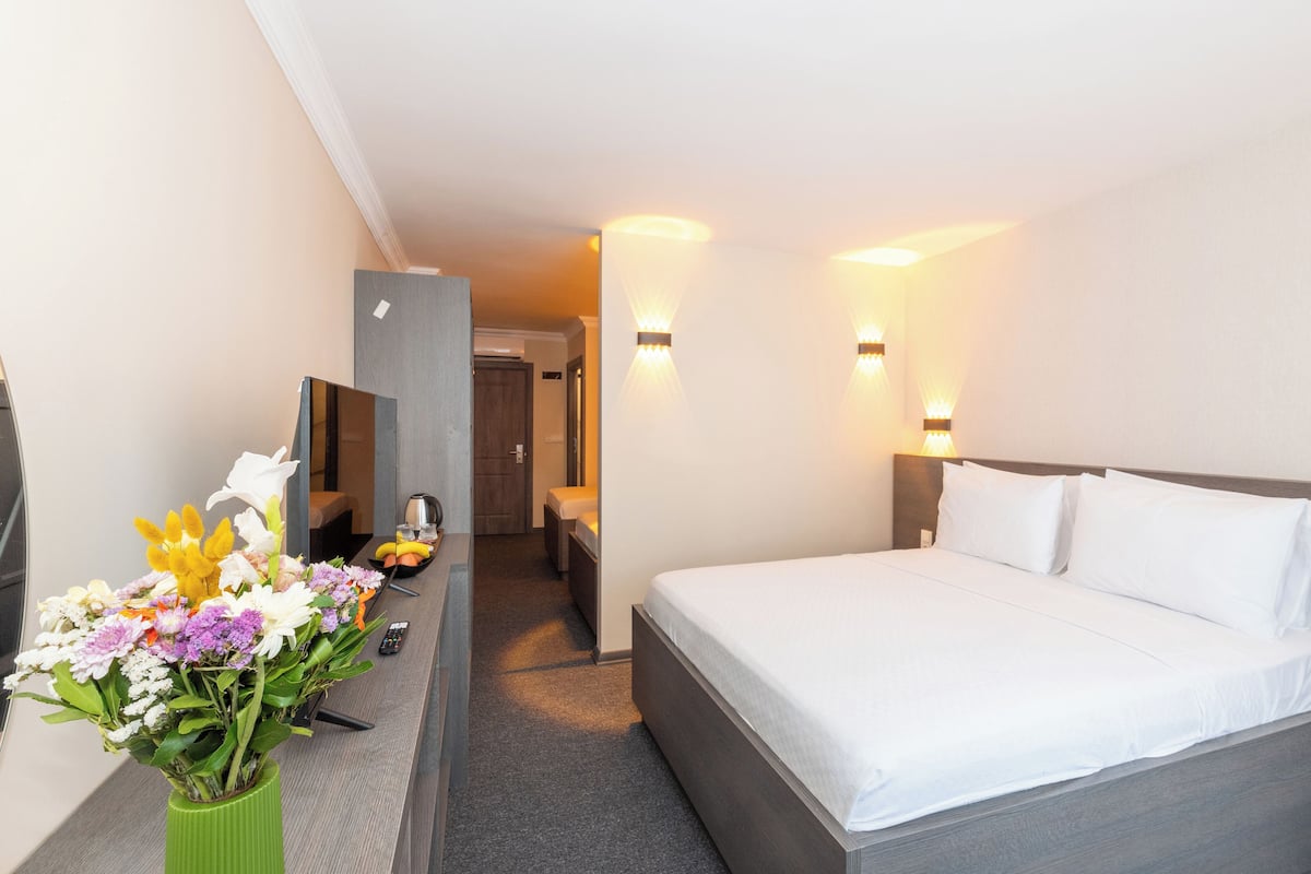 Quarto de hotel com uma cama, escrivaninha, cadeira, vaso verde com flores e televisão.