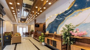 Vestíbulo de hotel con diseño moderno, que presenta una gran pared de mármol, mostrador de recepción de madera y una zona de estar con sofá y sillones.
