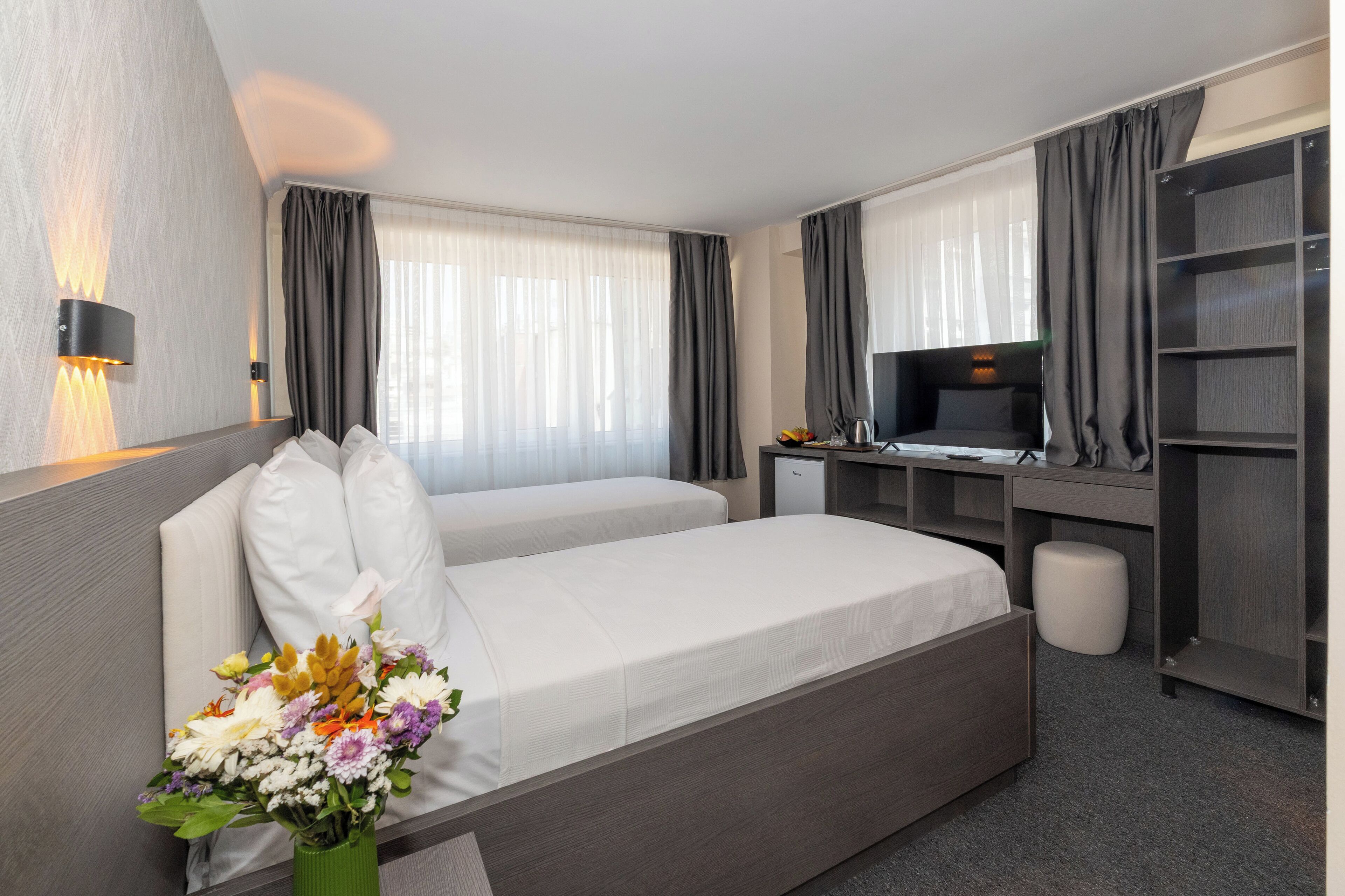 Ein Hotelzimmer mit einem großen Bett, einem Schreibtisch mit Fernseher, einem Bücherregal und einer Blumenvase.