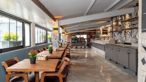 Un restaurante moderno con una larga mesa de madera, sillas acolchadas y una zona de cocina con encimeras de mármol.