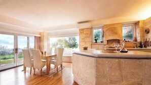 A spacious kitchen with a stone island, large windows, and a dining area with chairs.