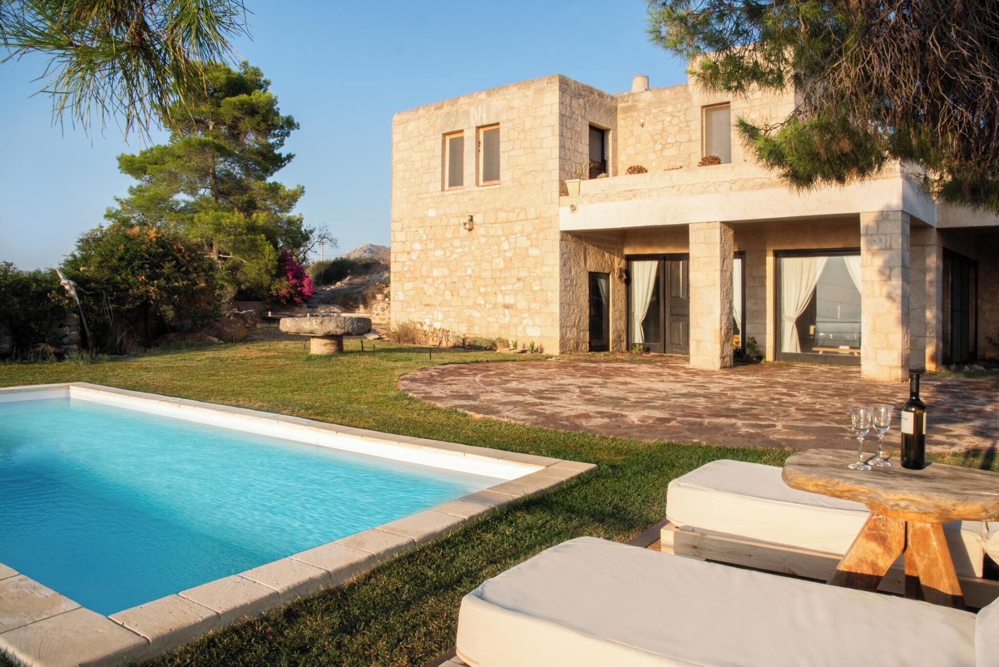 A modern stone house with a swimming pool, outdoor seating, and a patio area.