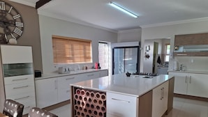 A modern kitchen with white cabinets, a central island, and a large clock on the wall. - Luxurious & Spacious
Swakopmund Accommodation (Swakopmund)