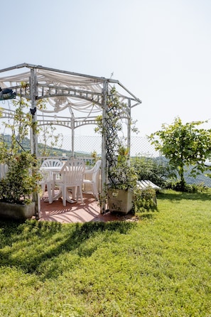 A gazebo with white chairs and a table, surrounded by greenery and a view of the sea. - Suite Al Pian Apartment with Private Pool, Wi-Fi, and Air Conditioning (MEZZANE DI SOTTO VERONA)