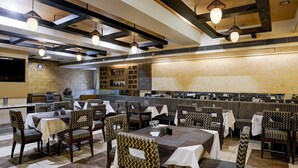 A restaurant with booths and tables, patterned chairs, and hanging pendant lights. - Suite Hotel Harmony (Rajkot)
